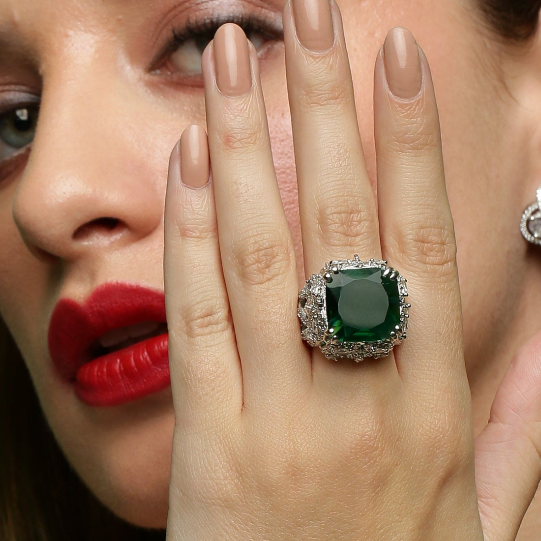 Elegant woman wearing an emerald gemstone statement ring with white stones, luxury designer jewellery close-up hand shot.