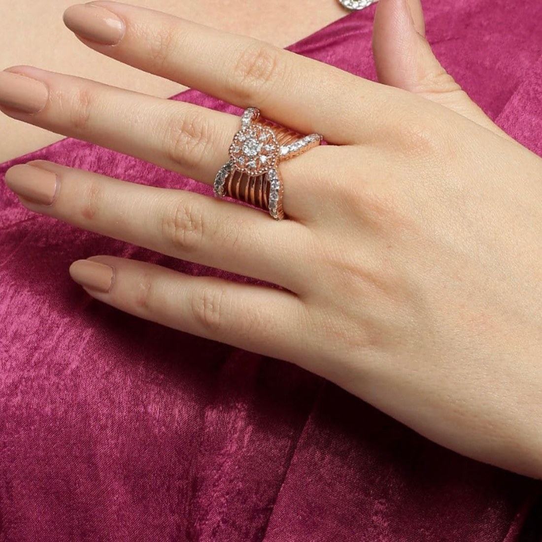 Hand wearing a rose gold ring with a diamond on a pink fabric background